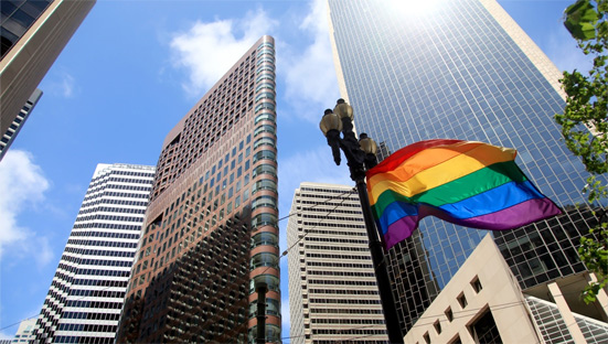 A rainbow flag flying outdoors, in front of skyscrapers