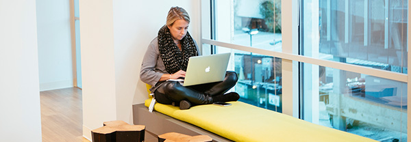 A woman in a corner chaise lounge with a laptop