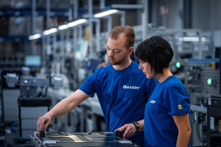 Man and woman in orange shirt and overalls conversing in manufacturing plant