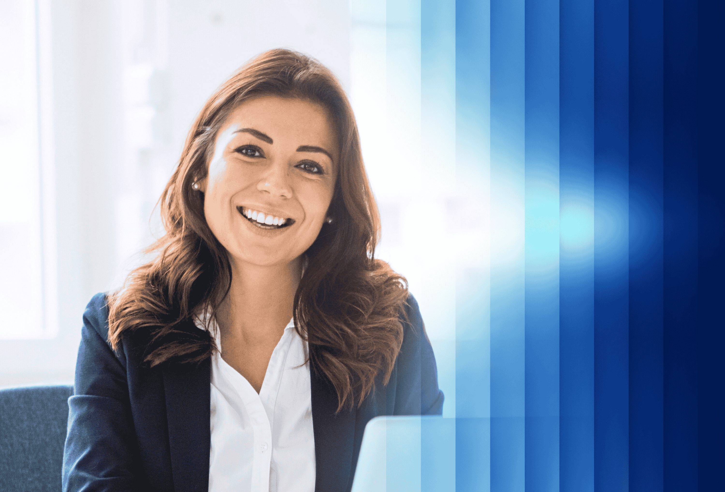 A woman smiling while sitting at a desk, focused on her laptop and working diligently.