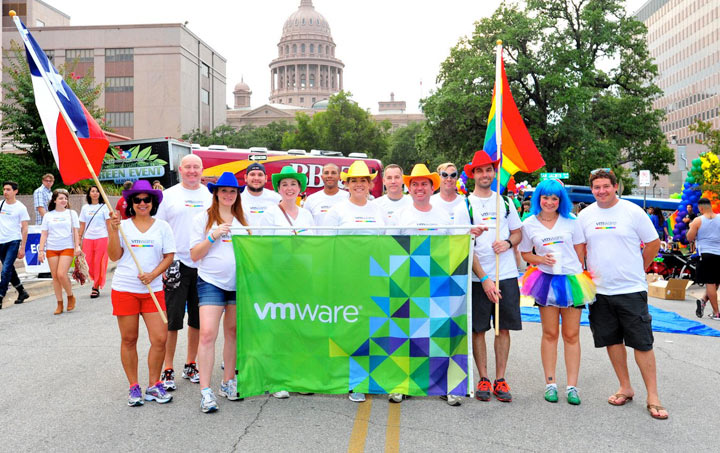 Employees with colorful hats and VMware banner hold Texas and rainbow flags at a pride parade in Texas.