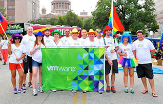 Employees with colorful hats and VMware banner hold Texas and rainbow flags at a pride parade in Texas.