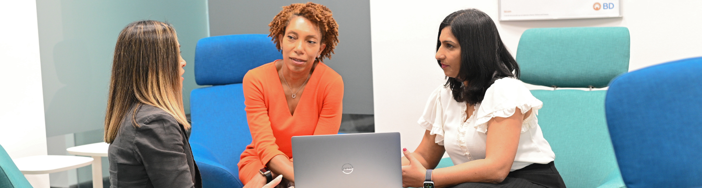 Three women talking around a table with a laptop
