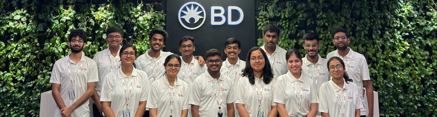 BD interns smiling at the camera in front of a wall with plants