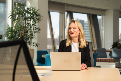 Smiling woman sits at desk in front of her laptop