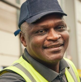 Smiling man in safety vest and cap near industrial area.