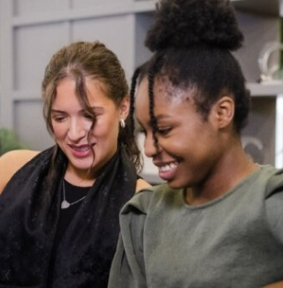 Two women smiling and looking at a laptop together.