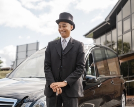 Man in top hat standing by a black hearse