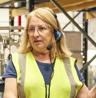 Two warehouse workers in vests talking on headset.