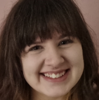 Smiling woman with bangs standing against pink wall.