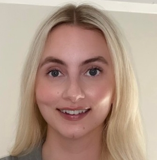 Smiling woman standing indoors against light wall.