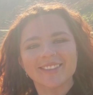 Smiling woman outdoors with sunlight in the background.