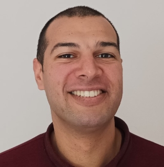 Man smiling in front of a plain light wall.
