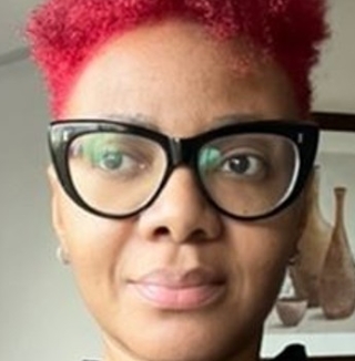 Woman with red hair and glasses near window.