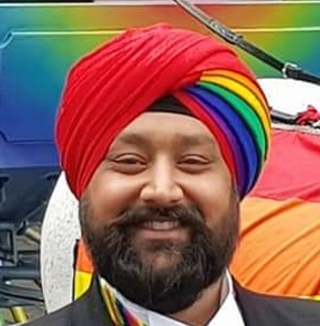 Man in rainbow turban smiling beside pride carriage.