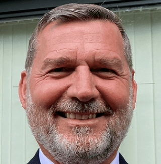 Smiling man standing outside a building entrance.