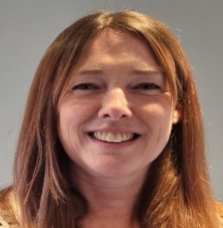 Smiling woman with long hair in front of gray wall.