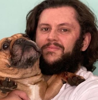 Man with beard holding a brown French bulldog.