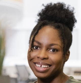 Smiling woman in an office setting with plants behind.