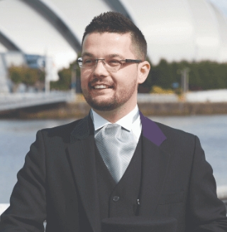 Man in formal wear standing by a riverside railing.