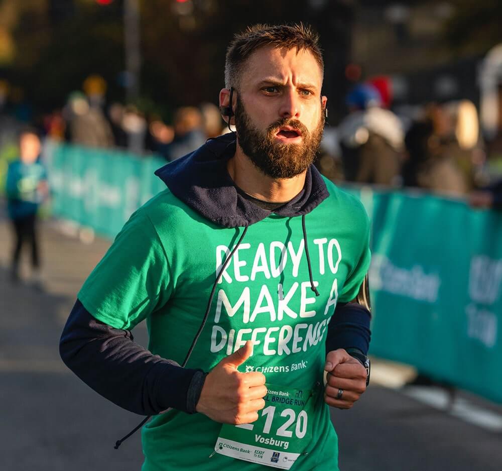 Male employee running in a charity race, wearing a green 'ready to make a difference' Citizens t-shirt