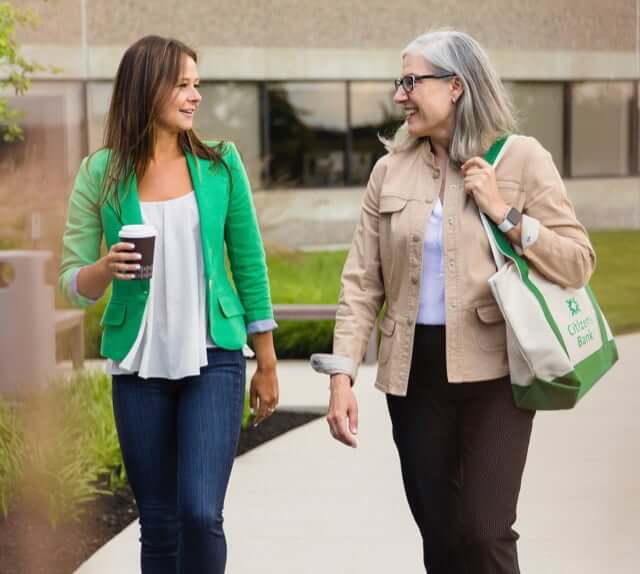 Young female employee chatting with an older female employee while walking outside an office building