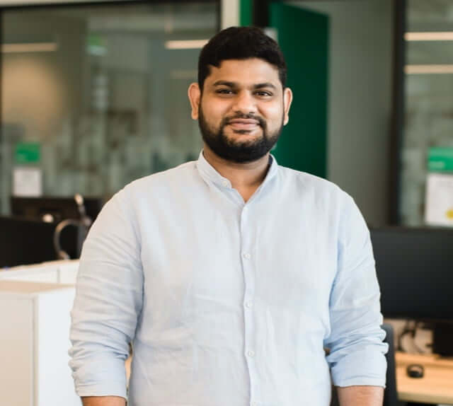 Indian male employee wearing a collared shirt and standing inside an office