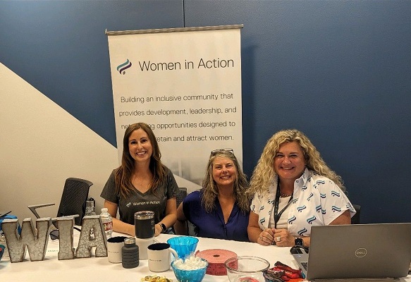 Three women pose at a Women in Action Employee Resource Group table.