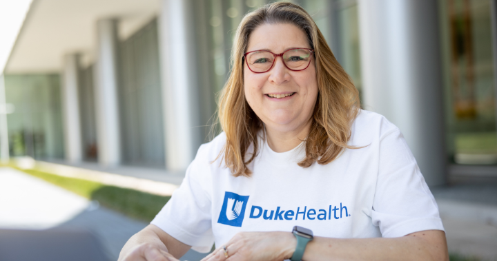 Women in Duke Health shirt smiling while studying on the Duke University Hospital campus.
