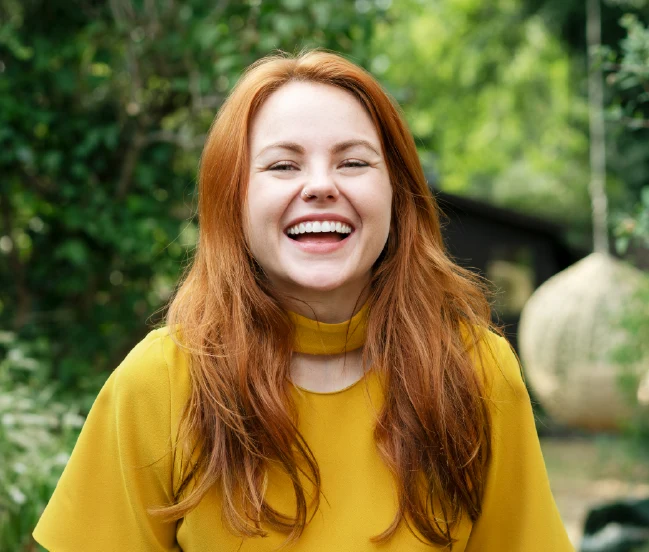 Young woman with red hair smiling at the camera in a forest setting