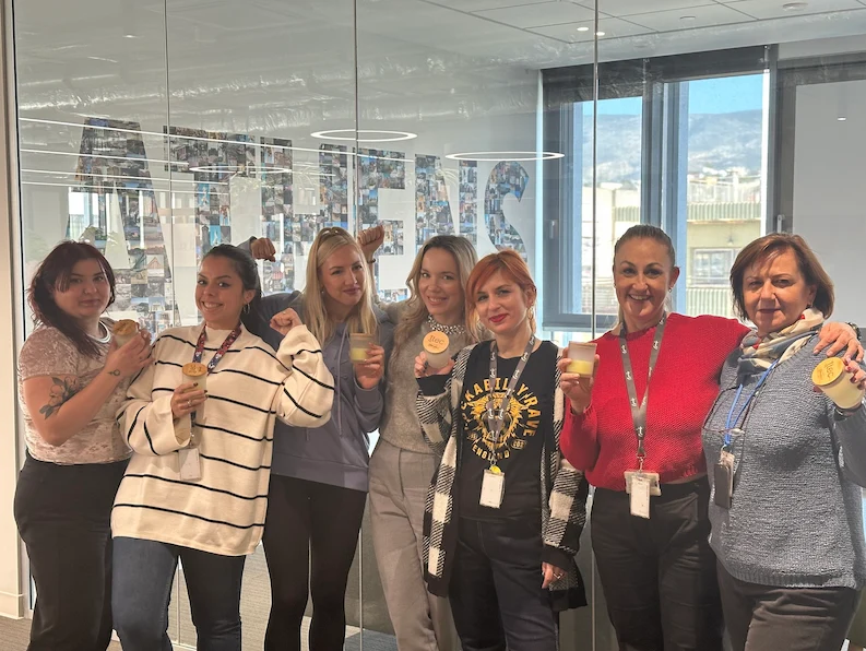 team of women at TTEC Athens smiling and proudly holding TTEC tokens, celebrating team spirit and success.
