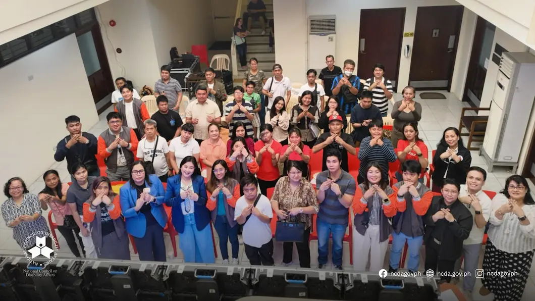 Job fair organizers and participants, including persons with disabilities, all smiling and holding up the NCDA hand sign.