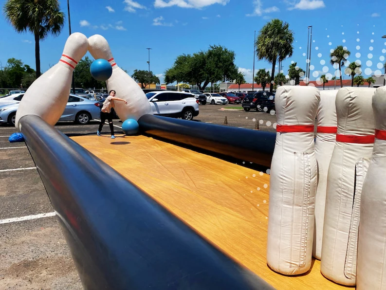A person inside a giant inflatable bowling alley, throwing the ball towards oversized pins in an outdoor game setup.