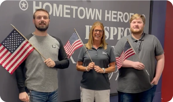 Three people holding American flags in front of Hometown Heroes mural