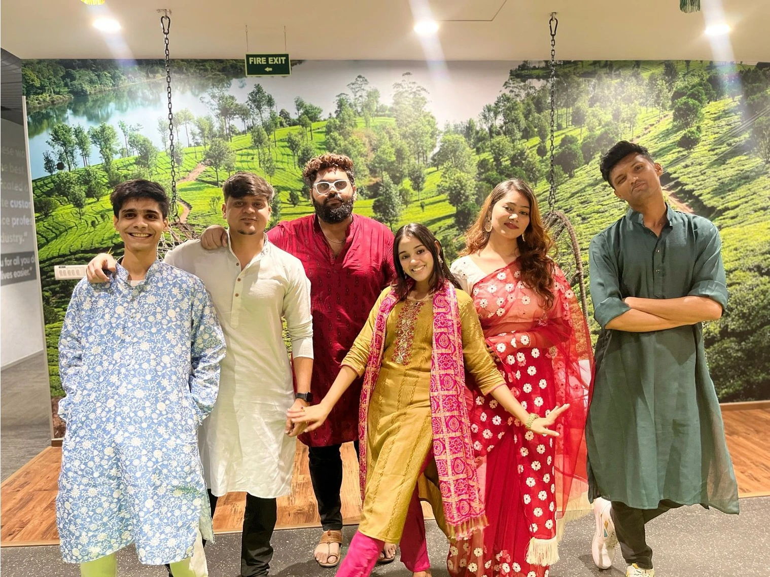 Group of young adults in traditional Indian attire posing and smiling indoors with a scenic wall backdrop