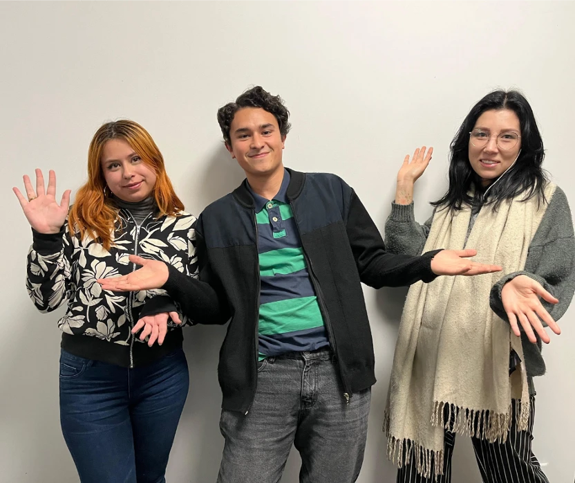 Three employees waving to the camera in front of a white wall.
