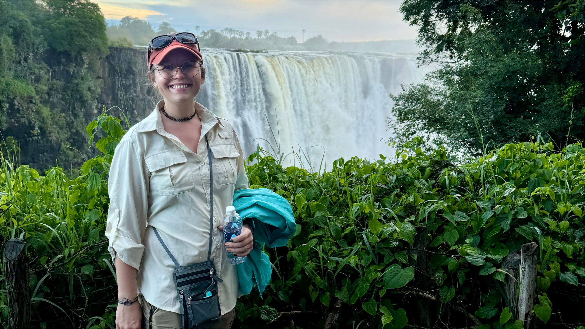 A smiling woman stands in front of a huge waterfall while on vacation in South Africa