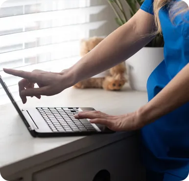 A person uses a laptop on a white desk, pointing at the screen with one hand and resting the other on the keyboard.