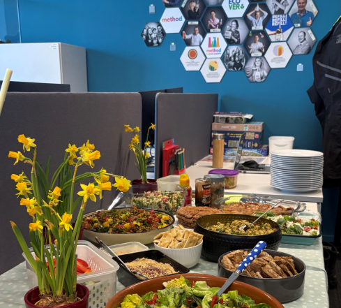 Table covered in potluck food dishes with flowers and team photos in the background
