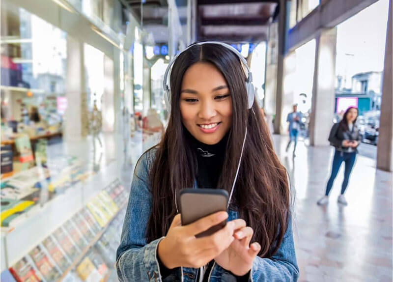 young brunette girl listening to music on her phone as she walks past the bookstore