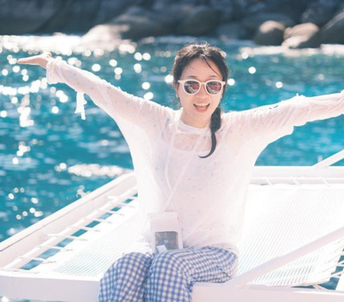 一位女士戴着墨镜高举双手坐在海边