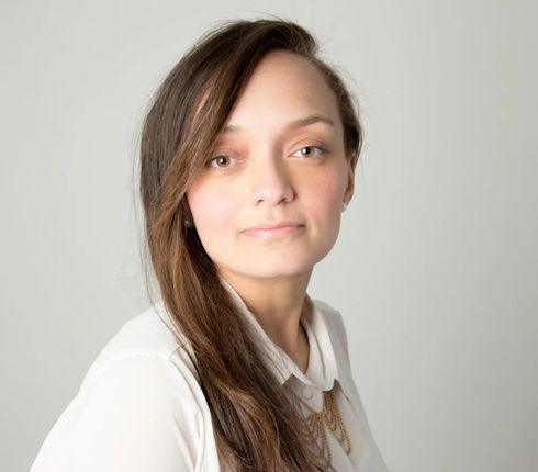 Diana, a Columbian woman with long brown hair is wearing a white blouse. She is looking directly at the camera with a subtle smile and warm expression. It's a professional headshot with natural lighting against a neutral background.