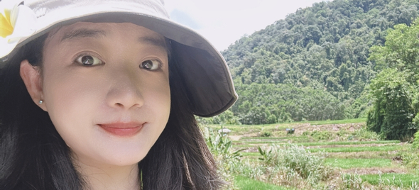 Iris, a Chinese woman, with long brown hair, is wearing a hat whilst standing outside in a field.
