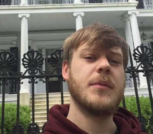 Lukasz, smiling in front of a house, wearing a red sweatshirt