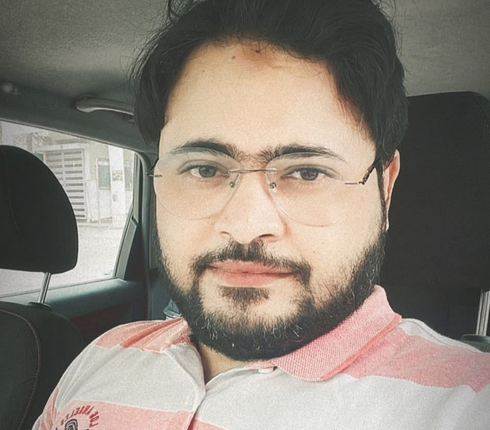 Shadaab - an Indian male, with dark hair, glasses and a beard. Wearing a pink and white button collared top.