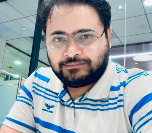 Shadaab, an Indian male, with dark hair, wearing glasses, with a dark beard. He is wearing a blue and white stripped top.