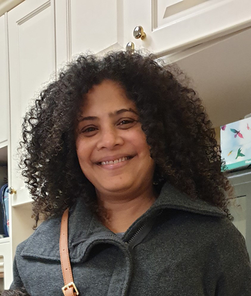 Chrishni smiling at the camera, open curly hair, wearing a gray coat.