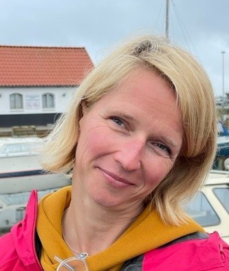 Headshot of Doreen, female European, chin long blond hair, a slight smile, outdoor clothes.