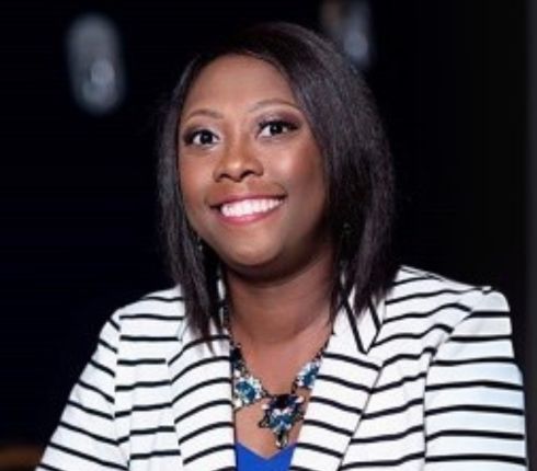 Marlayna, in a white and black striped jacket and blue undershirt, smiling at the camera