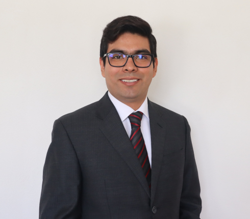Oscar, brown hair and wearing a black suit and glasses, smiling
